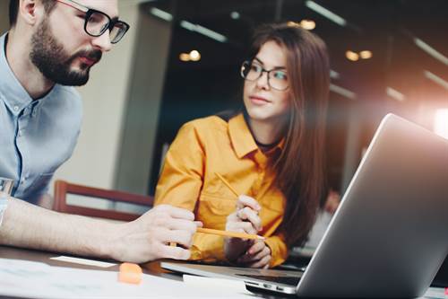 Business woman in glasses shows a colleague a project on a laptop. Discussing marketing plan. Laptop and paperwork on the table