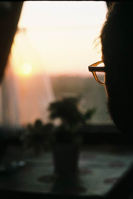 Silouette of man in glasses looing out a window at sun set dawn